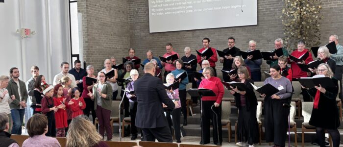People holding sheet music face a congregation and sing.